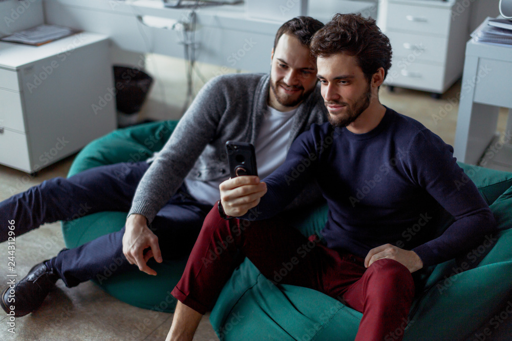 Obraz premium Two caucasian handsome young male friends taking selfie while sitting in the employer s office and waiting for the interview