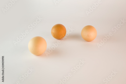 A group of three fresh eggs of different colors lie on a white background at a short distance from each other.