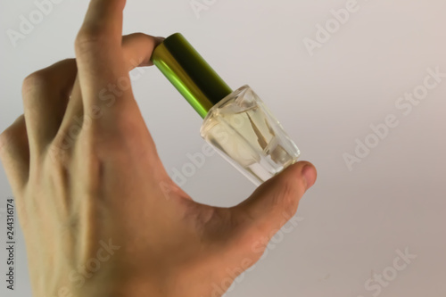 A bottle of transparent perfume with a green lid closed, a man holds a photo in his left hand with two fingers on a white background