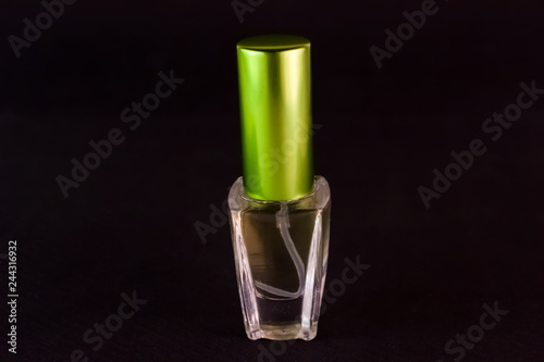 A bottle of transparent perfume with a green lid on the lid stands on a black background close-up photo