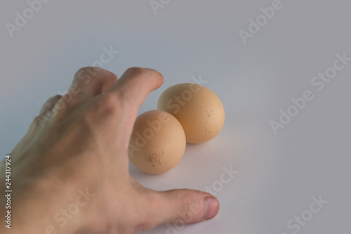 Human hand stretches to two chicken eggs lying on a white background