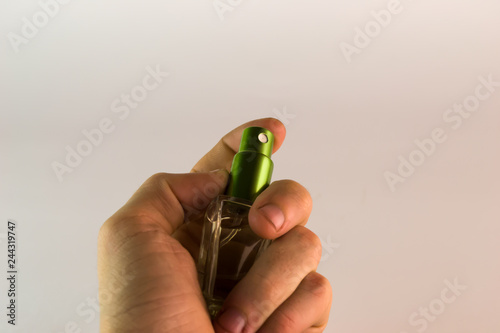 Transparent perfume bottle with green cap in man's left hand close up