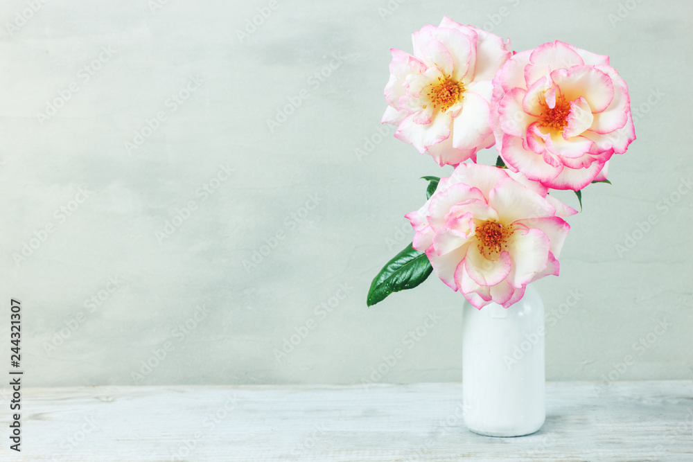 Roses in retro white vase on wood table on gray wall with copy space. Roses in retro white vase on wood table on gray wall with copy space.
