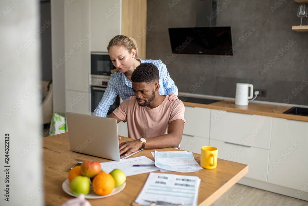 Young mixed race married couple having breakfast at the morning in kitchen and using laptop. Online shopping. Young mixed race married couple having breakfast at the morning in kitchen and using laptop. Online shopping.