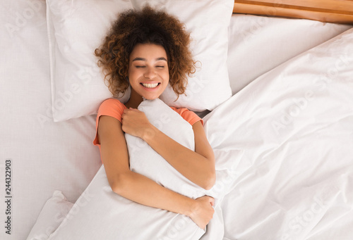 Young woman hugging pillow in bed, top view photo