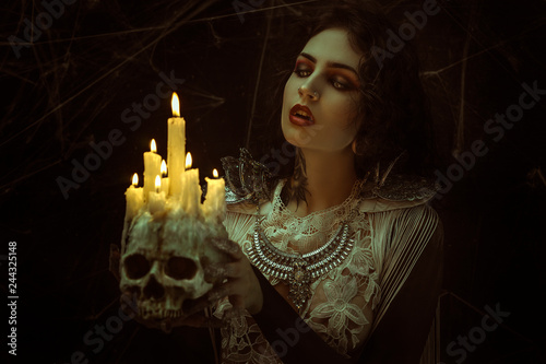 candles in skull, vampire, demonic woman dressed in white lace and silver jewelry. has fangs and thick brown hair photo