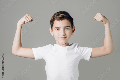 cute nice boy in white T-shirt shows biceps isolated on grey background. close up photo. studio shot. strength. power, sport and fitness