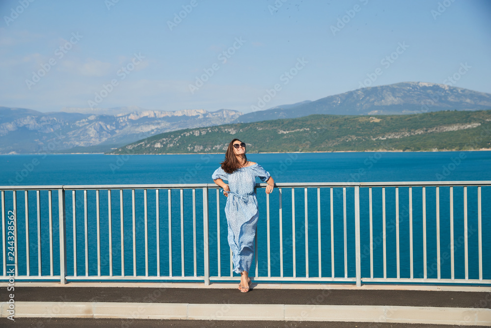 The beautiful girl in a blue dress and sunglasses poses on the bridge ...