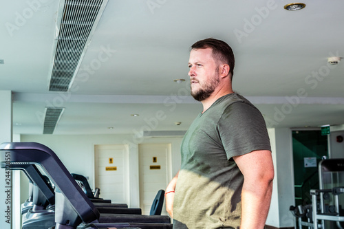 Sweating chubby man walking on running track, warming up on gym treadmill