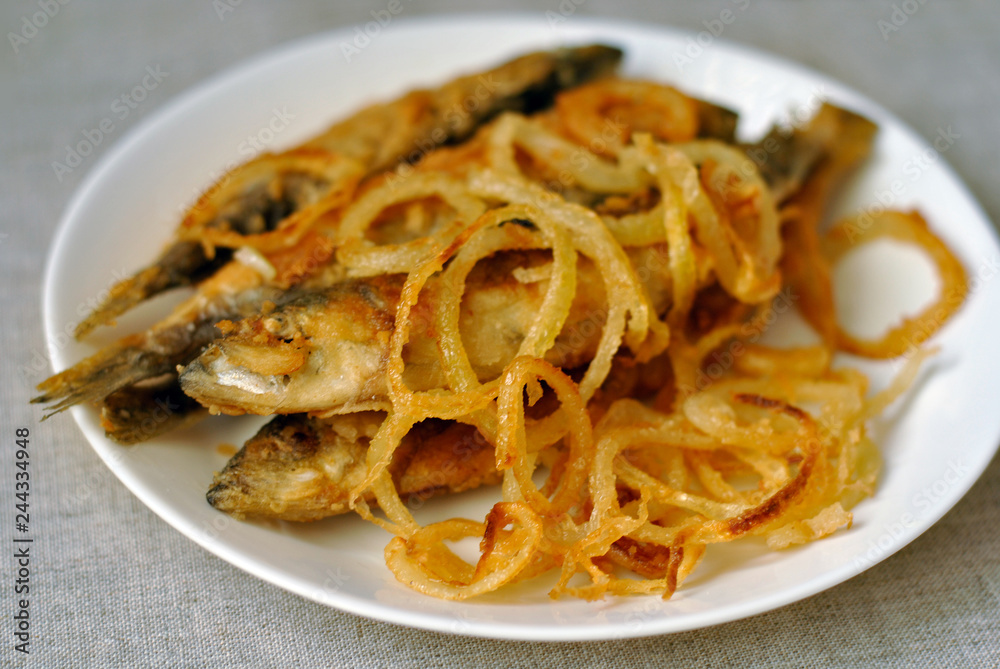 Fried fish and fried onions on a white dish. Close-up