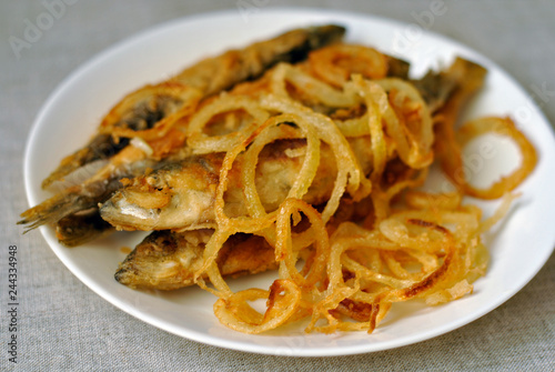 Fried fish and fried onions on a white dish. Close-up