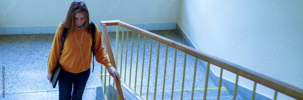 Obraz premium Young depressed lonely female college student walking down the stairs at her school, looking down. Education, Bullying, Depression concept.