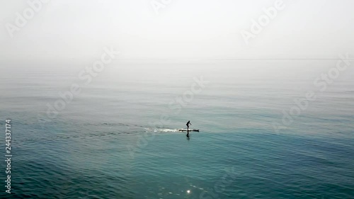 Aerial shot of a man on a stand up paddle, alone on a quiet sea, taken from a drone