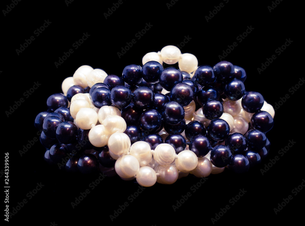 Two intertwined strands of natural white baroque and black pearls on black background Two intertwined strands of natural white baroque and black pearls on black background