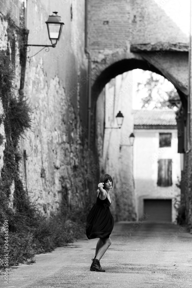 Farewell gesture from a young woman. She is alone in an old street of a french village.