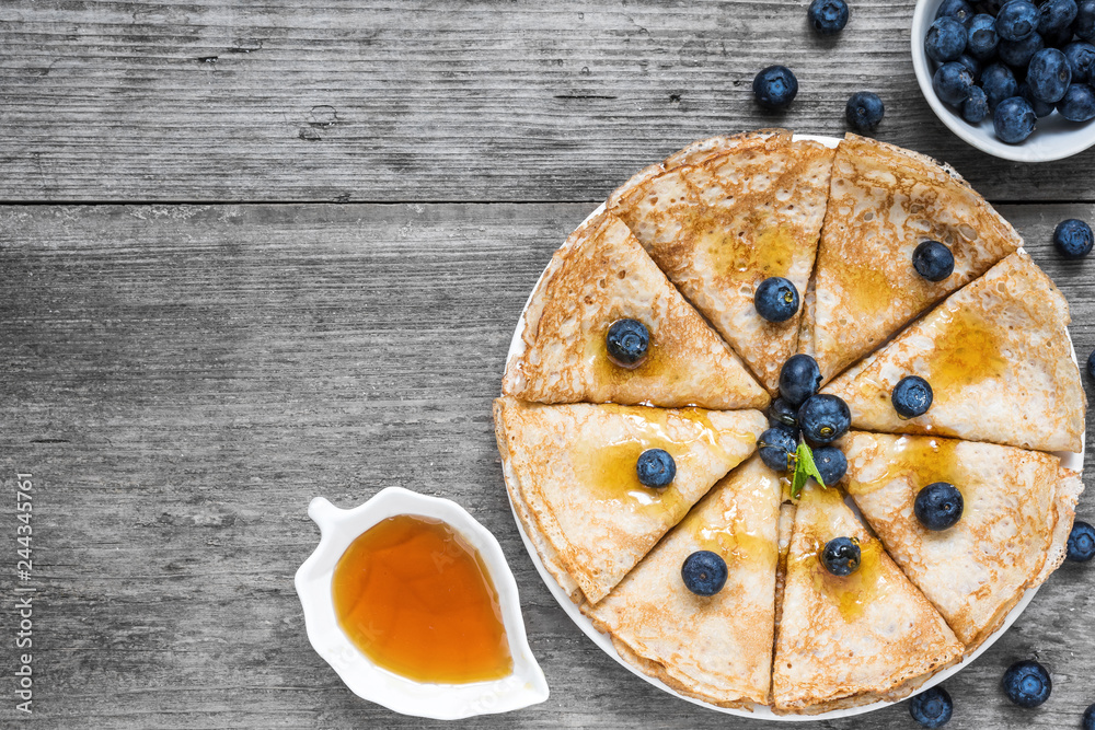 Pancakes with blueberries, maple syrup and mint leaf on top. Pile of thin homemade crepes with forest fruits. top view