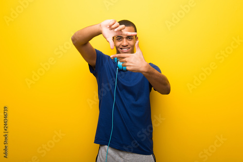 African american man with blue t-shirt on yellow background focusing face. Framing symbol