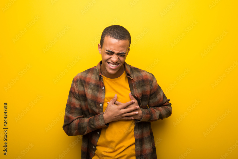 Obraz premium Young african american man on vibrant yellow background having a pain in the heart