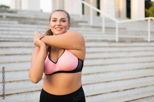Fényképezés Young beautiful plus size woman in pink sporty top and leggings stretching joyfu