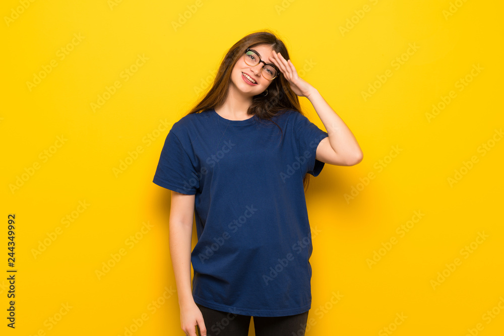 Young woman with glasses over yellow wall saluting with hand Young woman with glasses over yellow wall saluting with hand