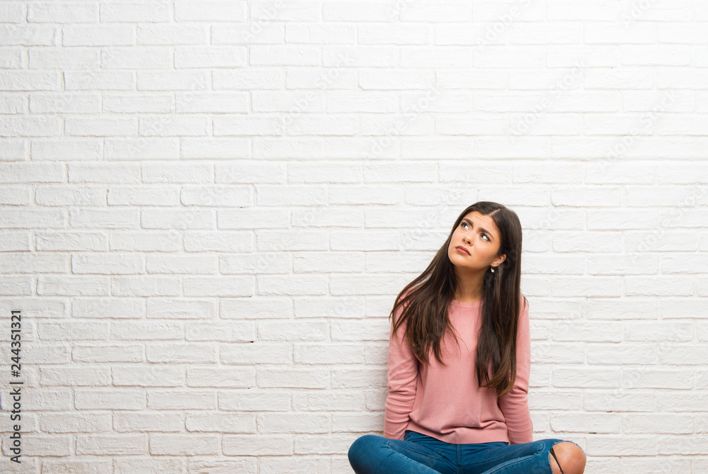 Teenager girl sitting on the floor in a room is a little bit nervous and scared pressing the teeth