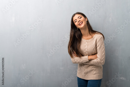Teenager girl with sweater on a vintage wall keeping the arms crossed while smiling