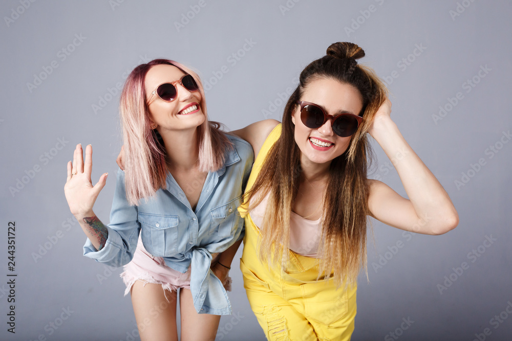 Carefree european woman in yellow denim overalls dancing with cheerful caucasian friend in blue shirt. Indoor photo of two happy girls in summer attires fooling around together. People, Friendship