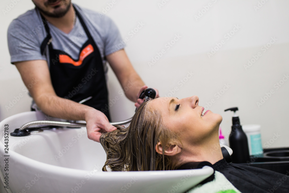 Hairdresser washing hair of a beautiful mature woman in hair salon.