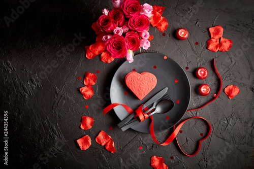 Valentines day, table setting and romantic dinner concept. Close up of plate with cutlery and rose petals on black stone background