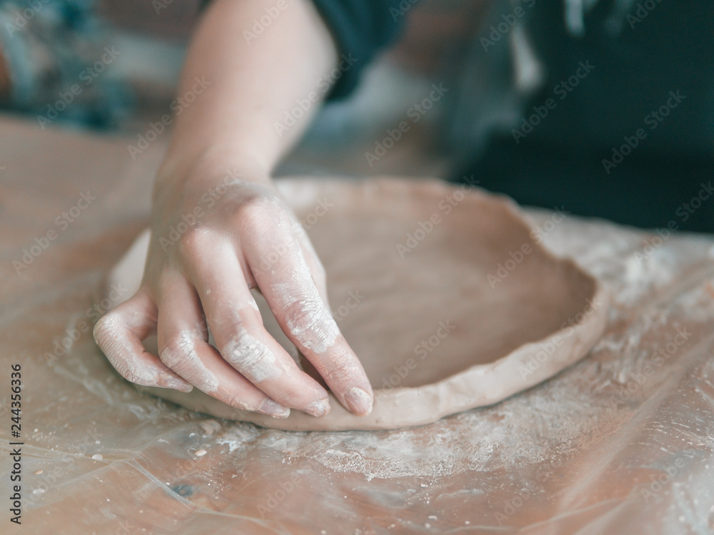 Female ceramist hands make trendy plate of brown clay. Close up view of fingers made fashion dessert flat plate on craft workshop. Female ceramist hands make trendy plate of brown clay. Close up view of fingers made fashion dessert flat plate on craft workshop.
