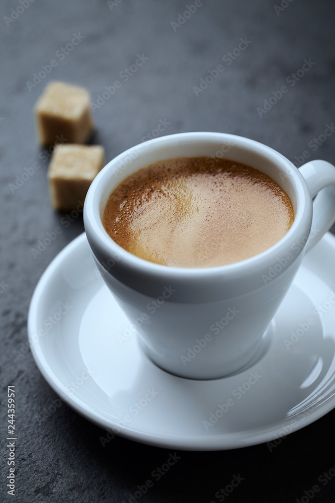 Cup of coffee and two brown sugar cubes on black stone background. Close up. Cup of coffee and two brown sugar cubes on black stone background. Close up.