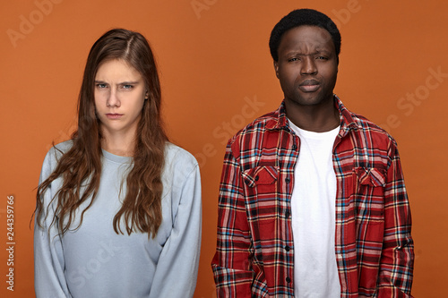 People, love, relationships problems and disagreement concept. Angry displeased white female and black male arguing having grumpy disappointed expressions, both frowning after quarrel or fight