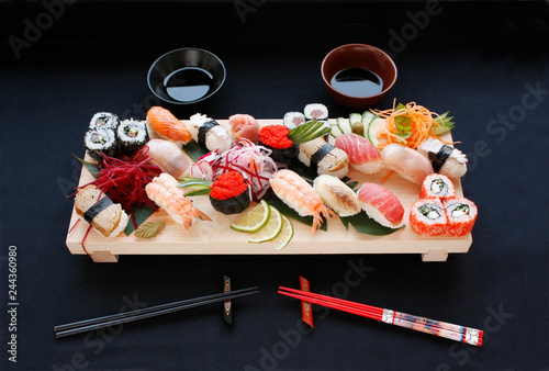 Assorted types of sushi on bamboo table with hashi chopsticks and shoyu. Sushi on black background. photo