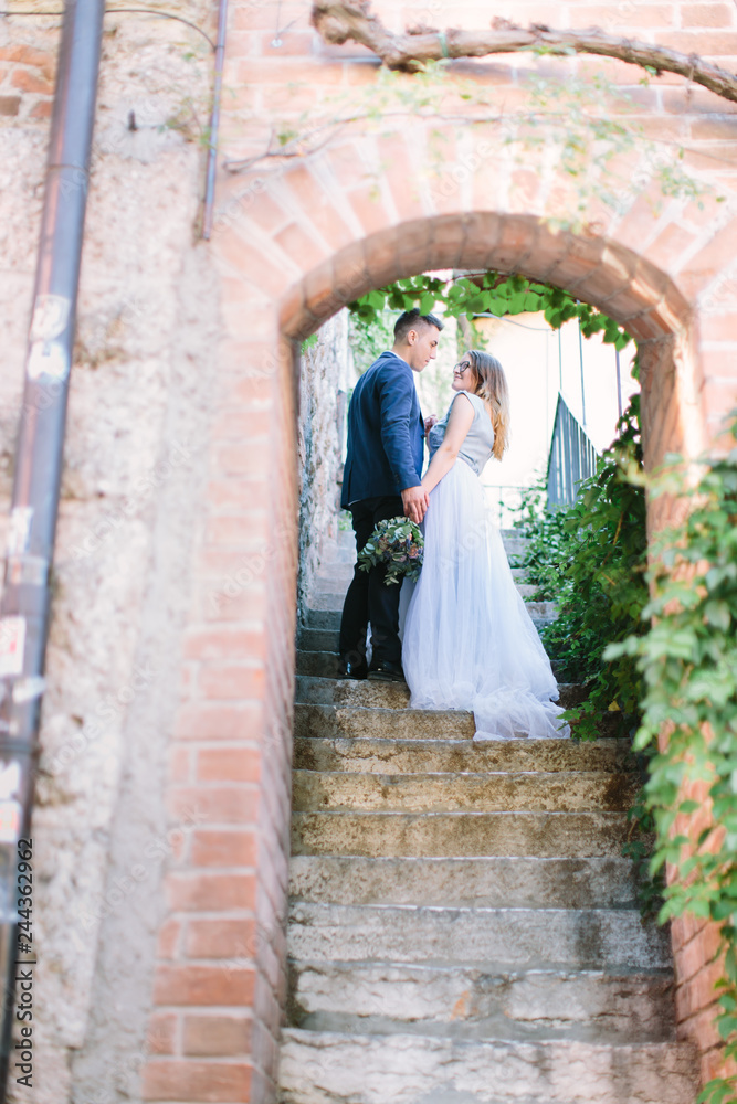 young beautiful couple standing and smiling on the background of old stairs and building in the city of Sirmione in Italy.
