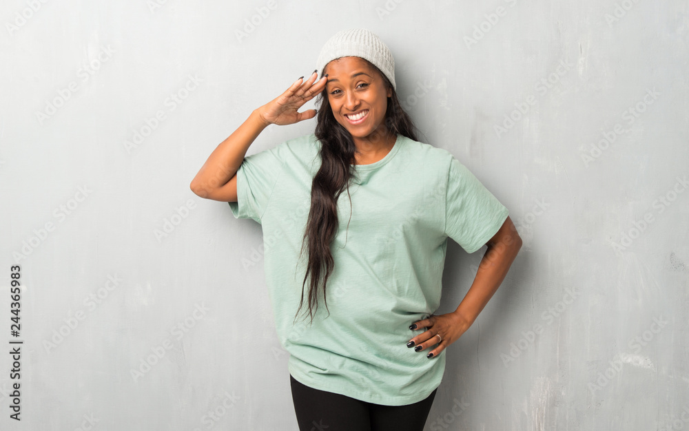 Young afro american woman on textured background saluting with hand