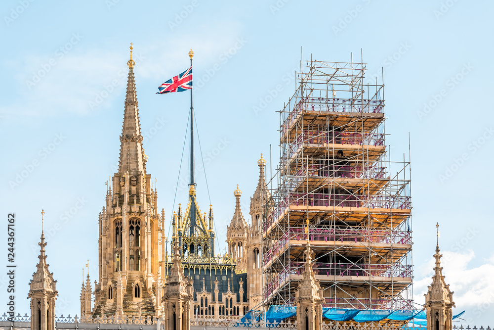London, UK closeup view of Big Ben clock bell tower construction scaffold scaffolding metal frame in city and Westminster Palace with flag