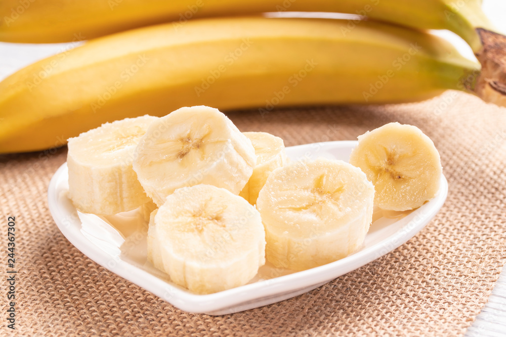Sliced and whole bananas on a white plate and old wooden roofing Sliced and whole bananas on a white plate and old wooden roofing