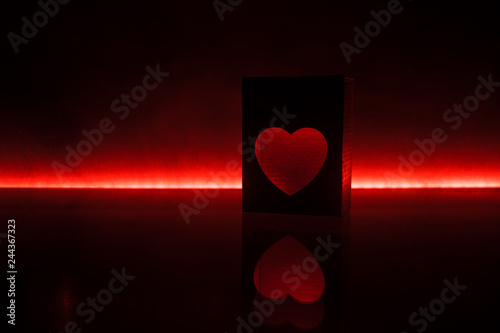 Blurred neon heart icon on a dark background. Copy space with red bright colorful heart on black background photo