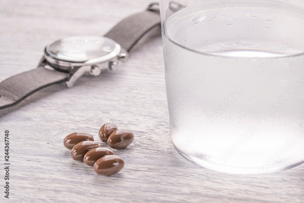 Misted glass of water and brown medical capsules on a white old wooden table. Wrist Watch