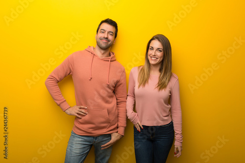 Group of two people on yellow background posing with arms at hip and smiling
