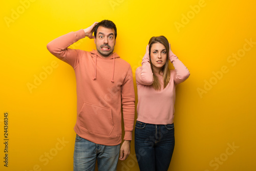 Group of two people on yellow background takes hands on head because has migraine