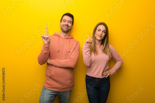 Group of two people on yellow background showing and lifting a finger in sign of the best photo