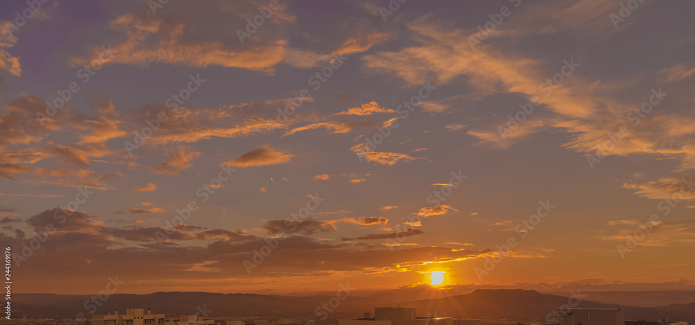 sunset scene with sun fall behind the clouds and mountains in background, warm colorful sky with soft clouds