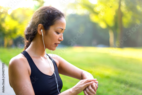 Sport asian woman listening to music with headphones while looking at watch outdoors