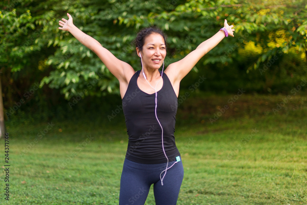 Asian woman stretching and listening to music with headphones outdoors
