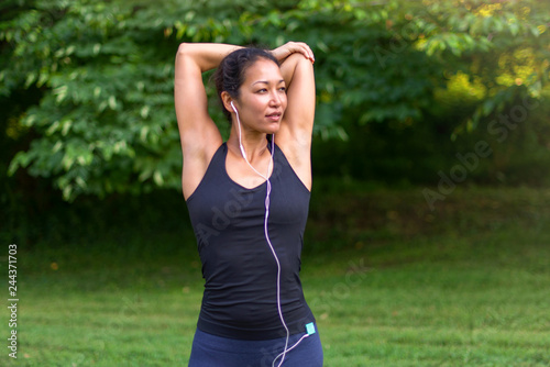 Asian woman stretching and listening to music with headphones outdoors