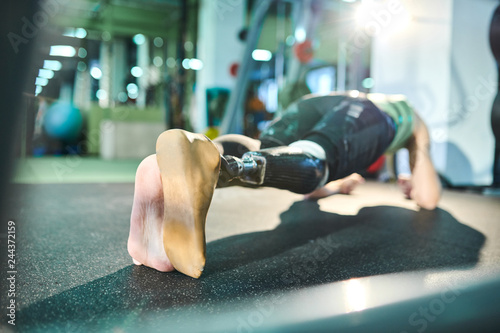 Fotografija Unrecognizable man of spirit with prosthetic leg practicing plank exercise in gy