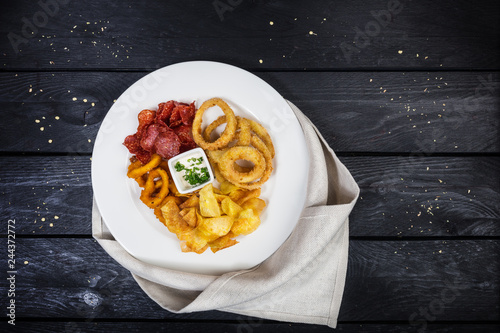 Rings of squid, onion rings, potato chips, salami chips with cheese sauce. photo