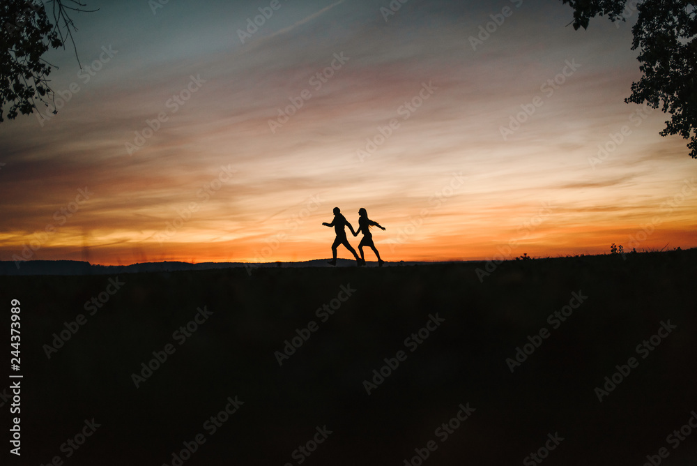 Young couple running by the sea and looking at the sun