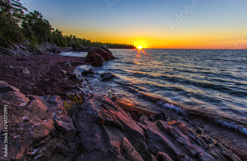 Rocky Coastal Sunset Landscape. Sunset over the horizon of Lake Superior with a rocky coastline in the foreground. Copper Harbor, Michigan, USA.